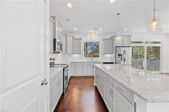 kitchen featuring dark wood finished floors, a kitchen island, appliances with stainless steel finishes, light stone countertops, and backsplash