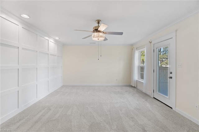 spare room featuring a decorative wall, light carpet, a ceiling fan, baseboards, and ornamental molding