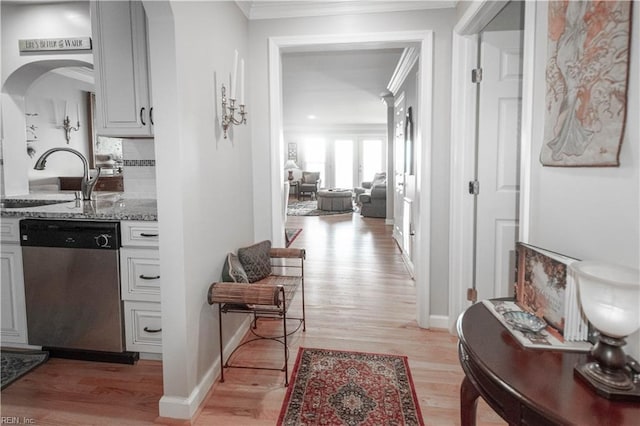 hallway with baseboards, arched walkways, ornamental molding, light wood-type flooring, and a sink