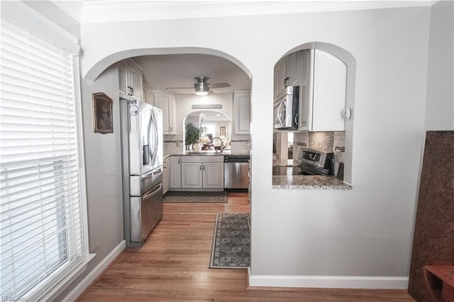 kitchen with dark wood-style floors, crown molding, stainless steel appliances, decorative backsplash, and ceiling fan