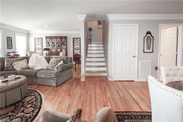 living room featuring light wood finished floors, baseboards, visible vents, stairway, and ornamental molding