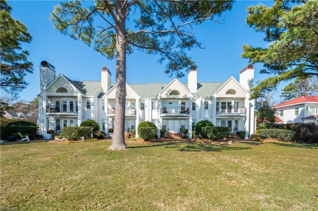 view of front of property with a chimney, french doors, a balcony, and a front lawn