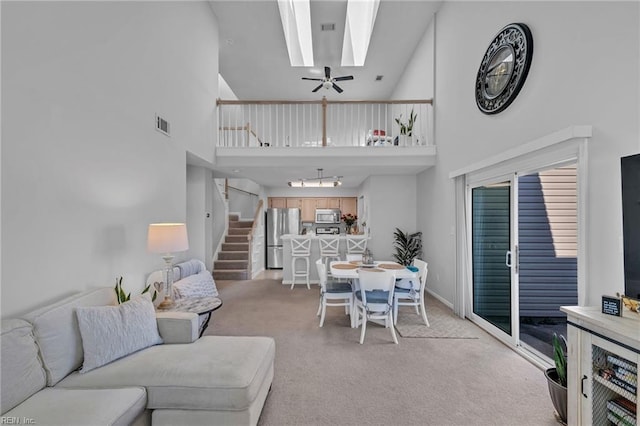 living area featuring light colored carpet, a high ceiling, a skylight, visible vents, and stairs