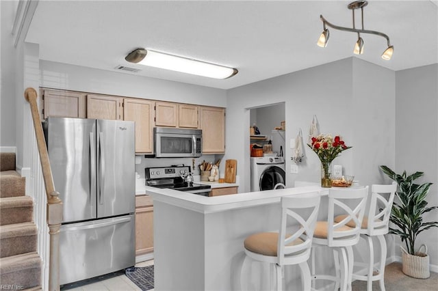 kitchen with washer / dryer, stainless steel appliances, light countertops, and light brown cabinetry