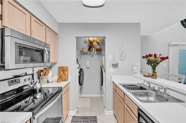 kitchen with a sink, light countertops, appliances with stainless steel finishes, light brown cabinetry, and washing machine and clothes dryer