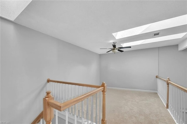 interior space featuring light carpet, a skylight, an upstairs landing, visible vents, and baseboards