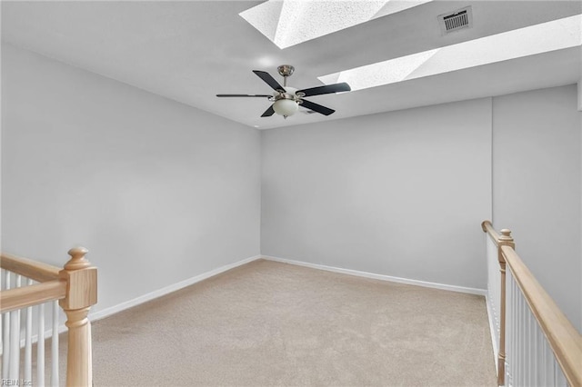 unfurnished room featuring light carpet, a skylight, baseboards, visible vents, and a ceiling fan