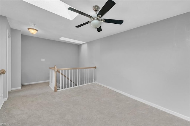 empty room with a skylight, ceiling fan, baseboards, and light colored carpet