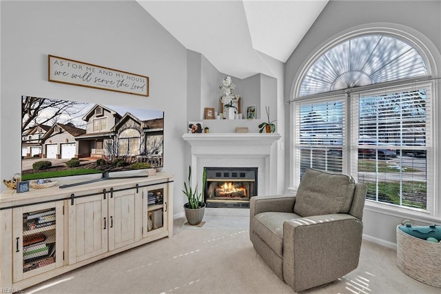 living area featuring light carpet, vaulted ceiling, a glass covered fireplace, and baseboards