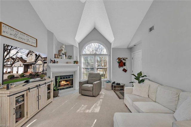 living area with high vaulted ceiling, a glass covered fireplace, visible vents, and light colored carpet