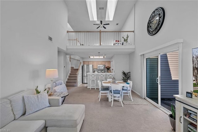 living area with light carpet, a skylight, a towering ceiling, visible vents, and stairway