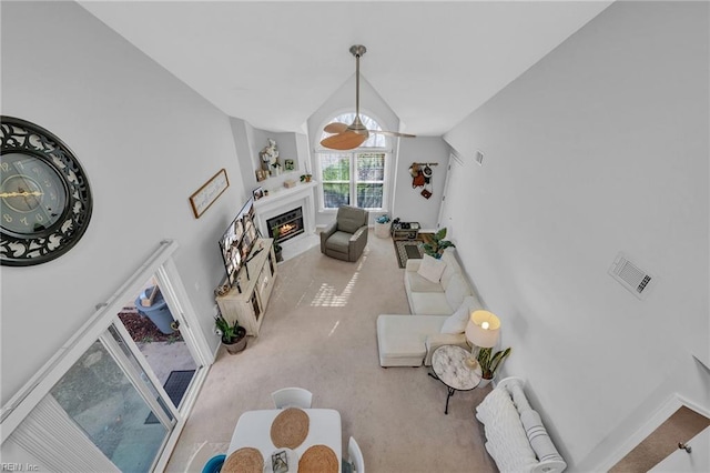 living area with a fireplace with flush hearth, lofted ceiling, light colored carpet, and a ceiling fan