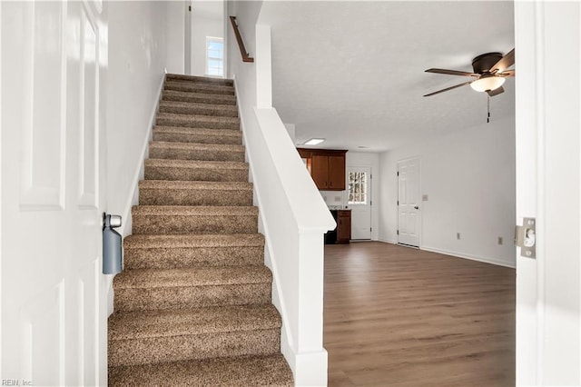 staircase featuring a healthy amount of sunlight, baseboards, a ceiling fan, and wood finished floors