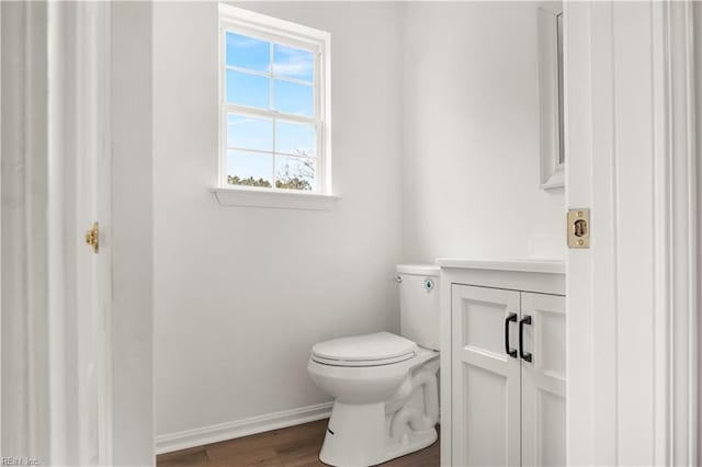 half bathroom featuring toilet, wood finished floors, vanity, and baseboards