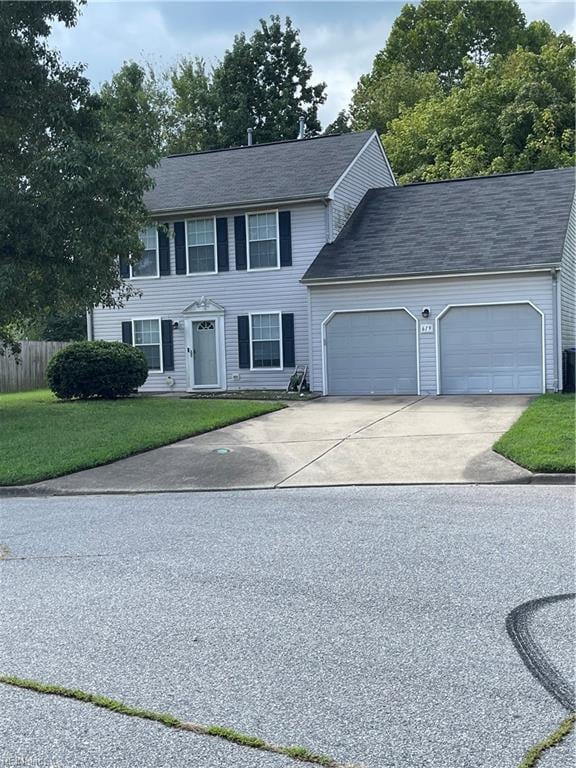 colonial-style house featuring an attached garage, driveway, fence, and a front lawn