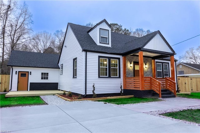 view of front of home with driveway, a porch, a shingled roof, and fence