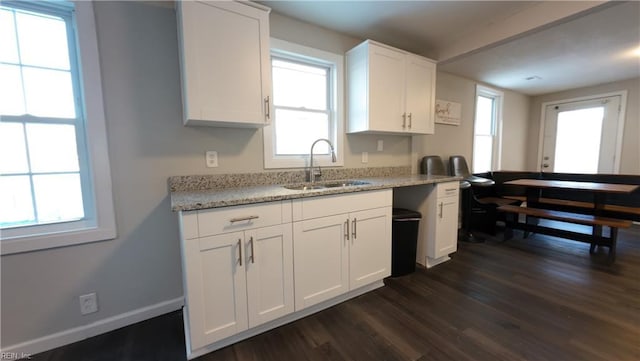 kitchen featuring dark wood-style floors, light stone counters, white cabinets, a sink, and baseboards