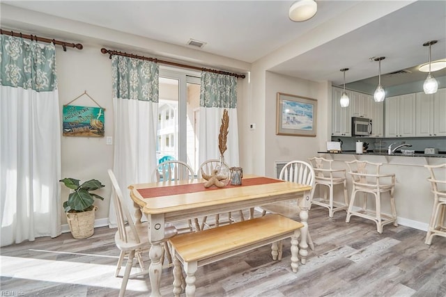 dining room with light wood-type flooring, visible vents, and baseboards