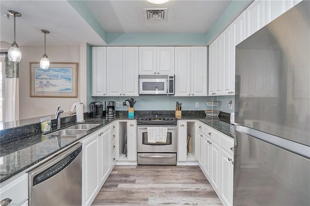 kitchen featuring stainless steel appliances, hanging light fixtures, white cabinets, a sink, and dark stone countertops