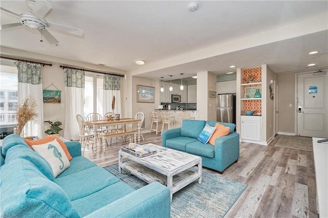 living room featuring light wood-type flooring, ceiling fan, baseboards, and recessed lighting