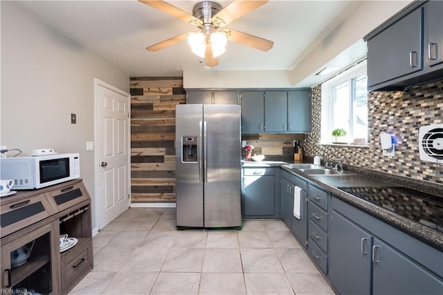 kitchen featuring stainless steel refrigerator with ice dispenser, dark countertops, backsplash, white microwave, and a sink