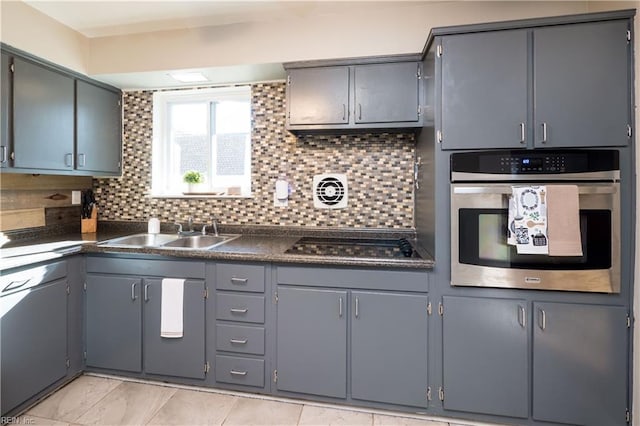 kitchen featuring dark countertops, stainless steel oven, a sink, and gray cabinetry