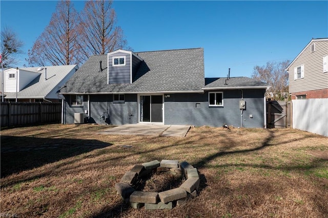 back of property with central AC unit, a fenced backyard, a fire pit, brick siding, and a patio area