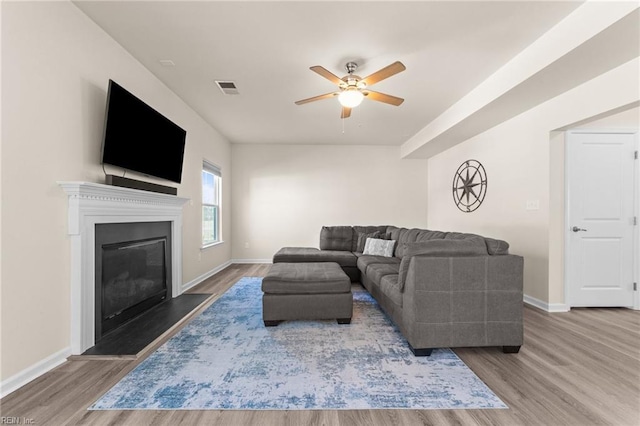 living room featuring a glass covered fireplace, wood finished floors, visible vents, and baseboards