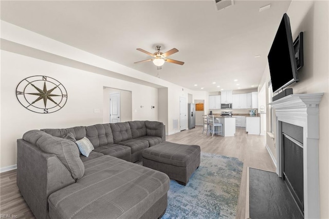 living room with light wood-style floors, ceiling fan, visible vents, and baseboards