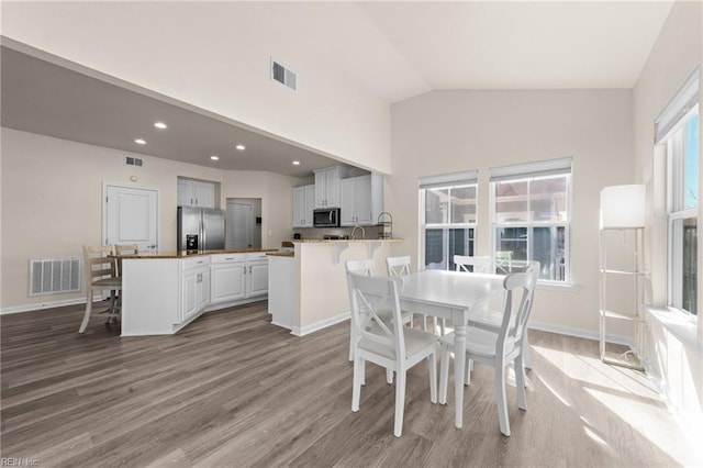 dining room featuring lofted ceiling, plenty of natural light, visible vents, and light wood-style flooring