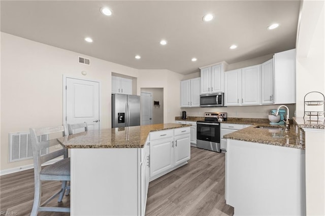 kitchen featuring a sink, visible vents, a kitchen island, white cabinetry, and appliances with stainless steel finishes