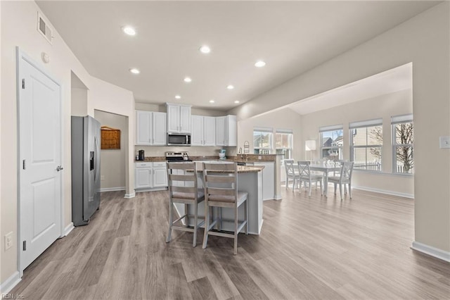 kitchen with visible vents, appliances with stainless steel finishes, light stone counters, a breakfast bar area, and white cabinetry