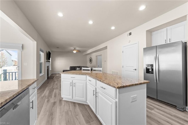 kitchen with light stone counters, appliances with stainless steel finishes, white cabinetry, and a center island