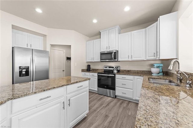 kitchen featuring light wood-style flooring, light stone countertops, stainless steel appliances, white cabinetry, and a sink