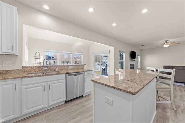 kitchen with a sink, white cabinetry, open floor plan, stainless steel dishwasher, and light stone countertops