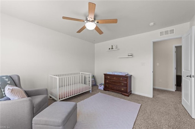 bedroom with a crib, visible vents, baseboards, light colored carpet, and ceiling fan