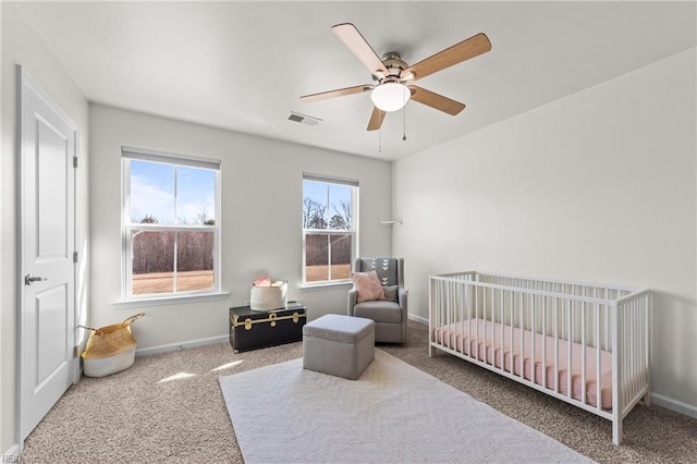 bedroom with a crib, baseboards, visible vents, ceiling fan, and carpet flooring