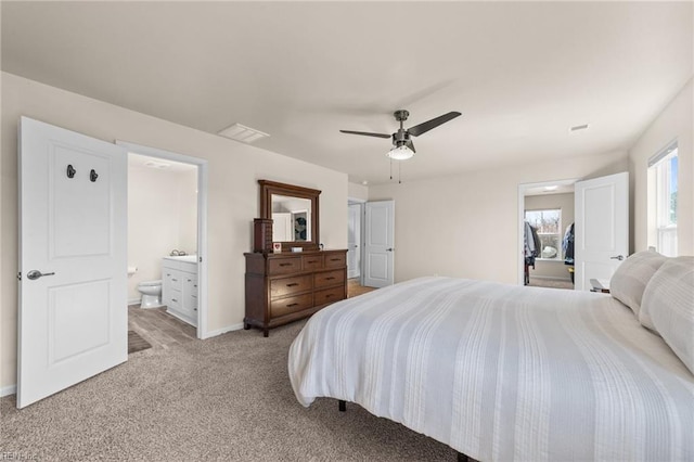 bedroom featuring baseboards, visible vents, a ceiling fan, light colored carpet, and ensuite bath