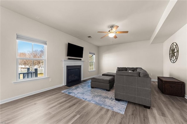 living room with ceiling fan, a fireplace with flush hearth, visible vents, baseboards, and light wood-type flooring