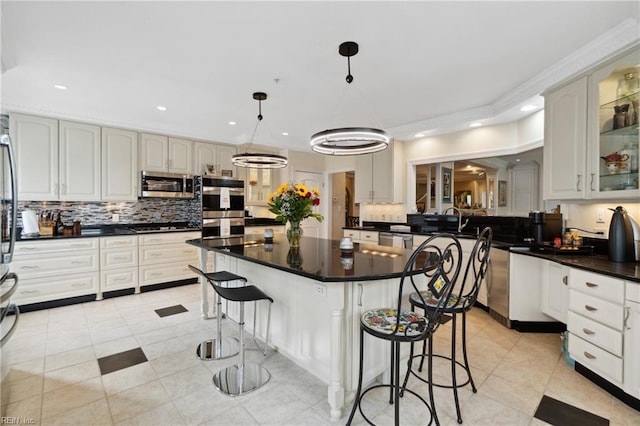 kitchen featuring stainless steel appliances, dark countertops, hanging light fixtures, a kitchen island, and a kitchen bar