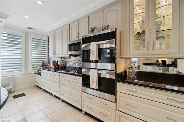 kitchen with light tile patterned floors, dark countertops, visible vents, appliances with stainless steel finishes, and glass insert cabinets