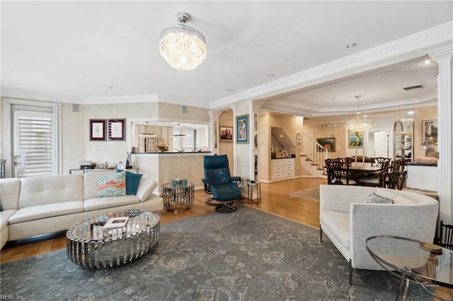 living area featuring a chandelier, wood finished floors, stairs, ornate columns, and crown molding