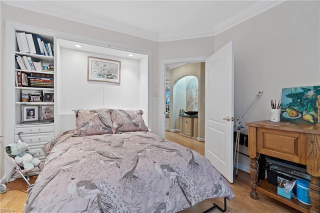 bedroom with arched walkways, light wood finished floors, and ornamental molding