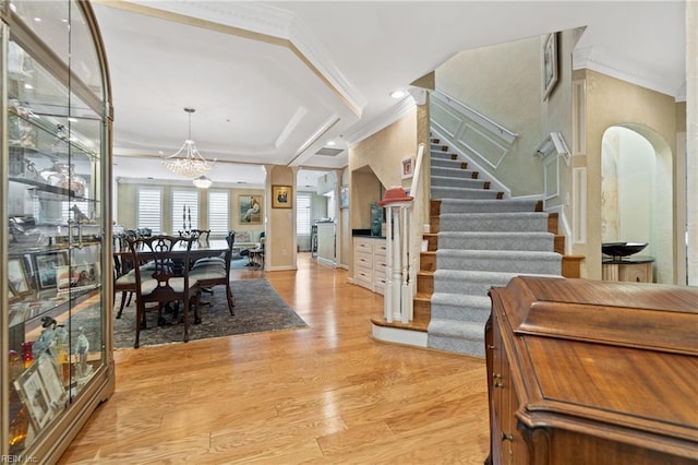 entryway with arched walkways, stairs, ornamental molding, light wood-type flooring, and an inviting chandelier