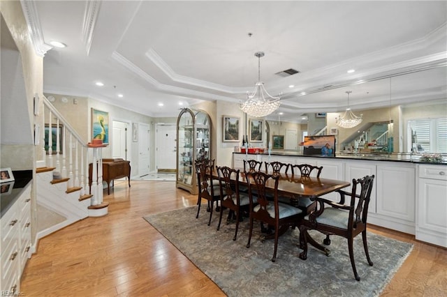 dining area featuring light wood finished floors, a raised ceiling, visible vents, ornamental molding, and stairs