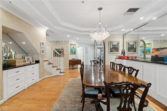 dining area with light wood-style flooring, visible vents, ornamental molding, stairway, and a raised ceiling