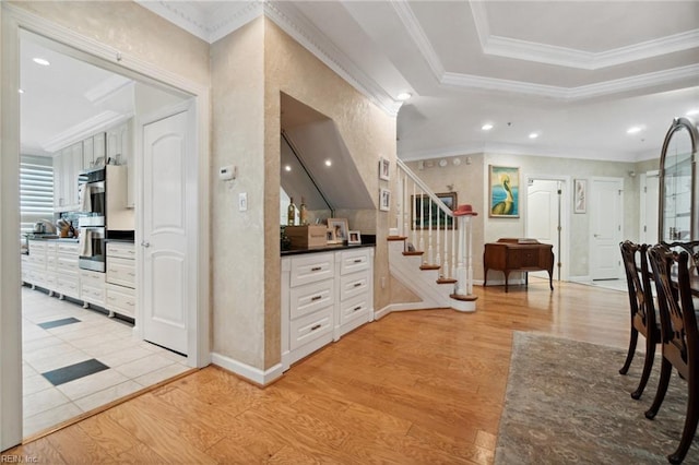 corridor with recessed lighting, ornamental molding, stairway, light wood-type flooring, and a raised ceiling