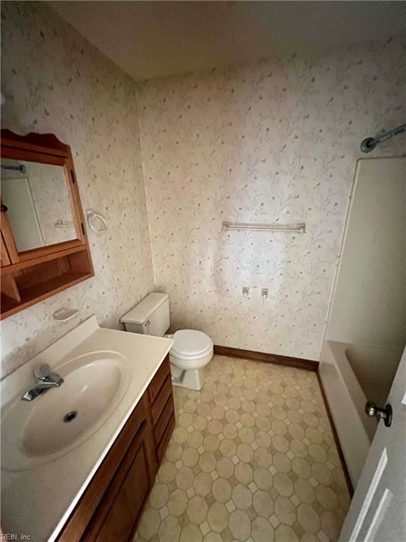 full bath featuring toilet, vanity, a tub, baseboards, and wallpapered walls