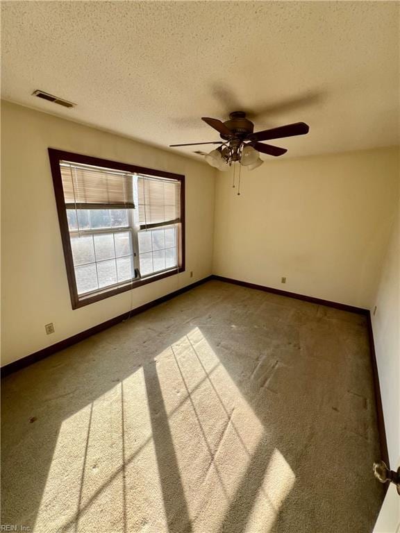 carpeted empty room featuring a textured ceiling, a ceiling fan, visible vents, and baseboards