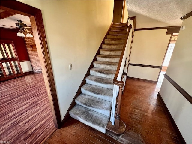 stairway with a ceiling fan, a textured ceiling, baseboards, and wood finished floors